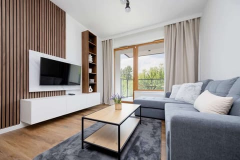 A modern living room with a sofa, coffee table, and wide window with curtains leading to a balcony.

