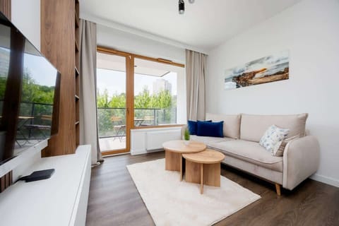 A modern living room with a sofa, coffee table, and wide window with curtains leading to a balcony.

