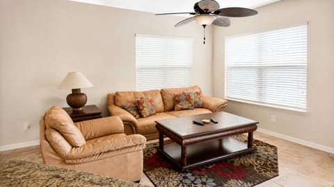 Comfortable living area with cozy sofa seating, ceiling fan, large windows, and a bright open feel.