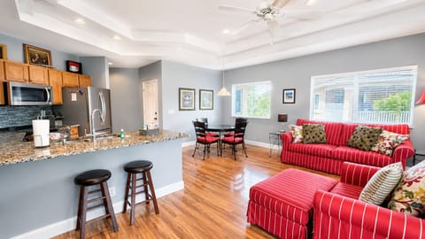 Bright open kitchen and living area with breakfast bar seating, wood-look flooring, cozy red seating, and plenty of natural light.