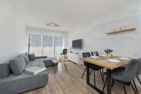 The living room with bright walls, wooden flooring, and a large window creates a space full of light and coziness.