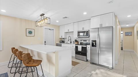 Cocoa Beach Kitchen | Bright coastal design featuring a waterfall island, leather stools, and modern stainless finishes.