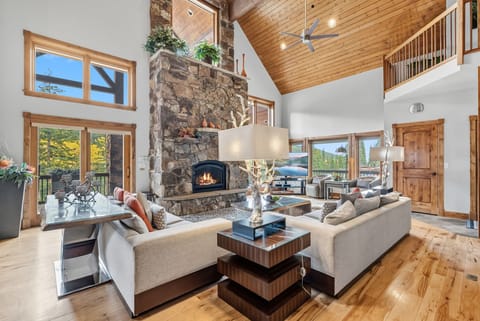 The great room boasts high ceilings, plenty of natural light, plush seating, and an impressive stone hearth fireplace. 