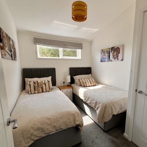 The twin bedroom features two single beds with a bedside cabinet and a table lamp placed between them. The room also includes a wardrobe with a shelf and hanging space for clothes. 