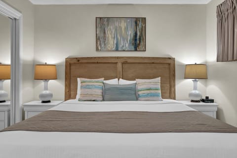 Sink into crisp white linens and plush pillows in your serene bedroom sanctuary, where warm lighting and coastal artwork create the perfect retreat.