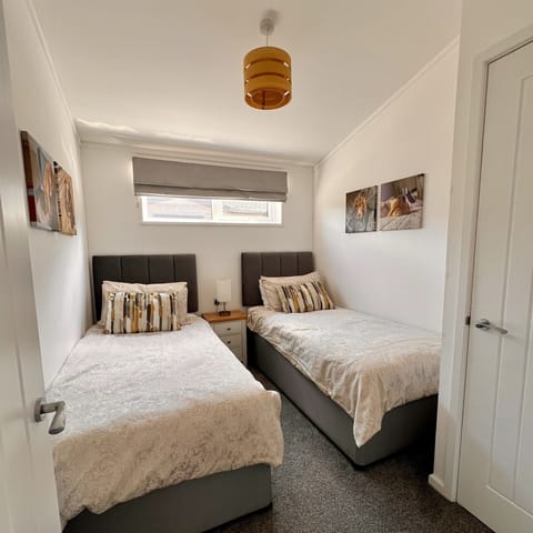 The twin bedroom features two single beds with a bedside cabinet and a table lamp placed between them. The room also includes a wardrobe with a shelf and hanging space for clothes.