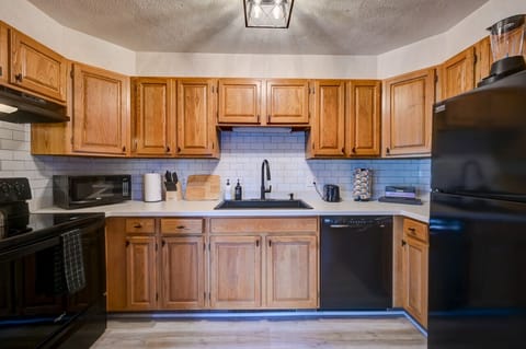 Fully equipped kitchen with warm wood cabinetry, modern black appliances, and all essentials for cooking a delicious family meal. Enjoy ample counter space, a coffee maker, and stylish subway tile.