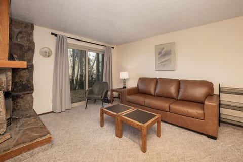 Sink into the leather sofa by your cozy stone fireplace, where forest views through sliding doors create your perfect retreat sanctuary.