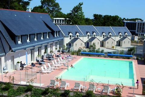 Aerial view of the pool terrace with white loungers, café seating, and a row of Breton slate-roofed cottages behind