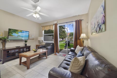 Cozy living room with leather sofas, flat-screen TV, and patio access to a lush garden view.