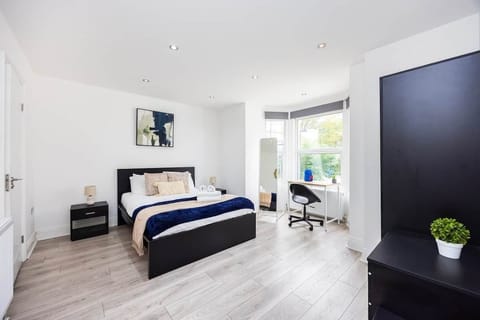 Spacious bedroom equipped with a double bed, dedicated workspace by the window, and full-length mirror. The room offers ample storage with bedside tables and a large wardrobe, all set within a bright, recessed-lit interior.