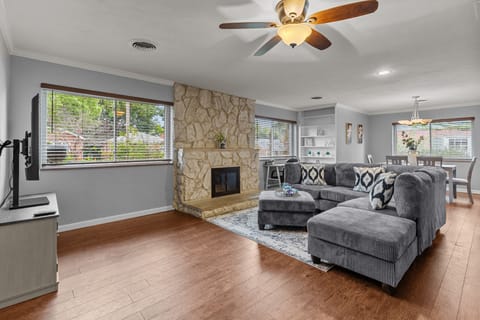 Open-plan living room with a gray sectional, stone fireplace, television, and dining area beyond.