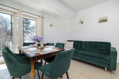 Bright dining area with green velvet chairs and large windows.