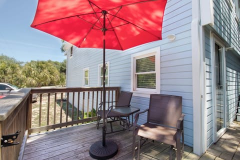 Sip your morning coffee or enjoy evening cocktails on this sunny private deck, shaded by a vibrant umbrella and surrounded by coastal greenery.