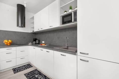 A compact kitchen with white cabinets and a sleek grey countertop. Built-in appliances and minimalist decor give it a modern feel.