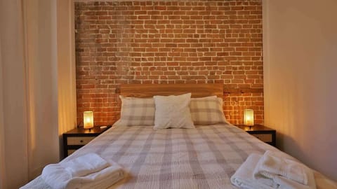 ✨ Signature Montreal Charm: Master bedroom featuring stunning original exposed brick and warm lighting.