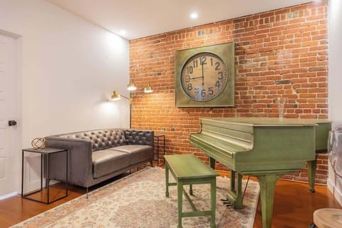 Cozy entertainment area with a brick wall backdrop, complete with a piano, wall clock, and comfortable couch.