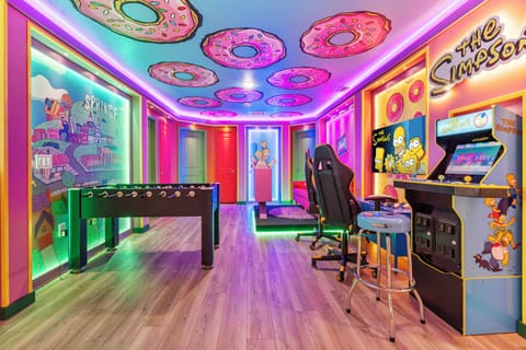 Step into a vibrant game room that promises hours of entertainment, featuring playful donut-themed decor and colorful LED lighting. Enjoy a foosball table and classic arcade games, all set against a backdrop of vivid artwork.