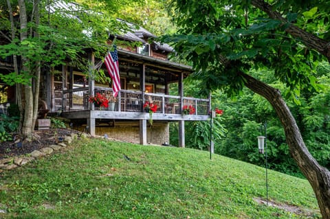 Elevated wooden porch with rustic railing, red flower pots, and American flag overlooking a grassy hillside.