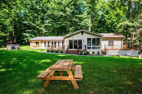 Expansive backyard with a wooden picnic table, surrounded by dense green trees and a beige vinyl-sided house.