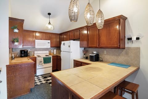 Cozy kitchen with rich wooden cabinets, tiled countertops, and modern lighting, offering a warm, functional space for cooking and gathering.