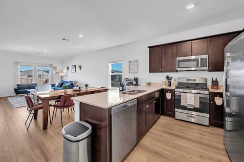 Spacious open-concept kitchen with stainless steel appliances, dark wood cabinets, and a large island with seating. Overlooks a stylish dining area and cozy living room—perfect for cooking, dining, and entertaining all in one inviting space.