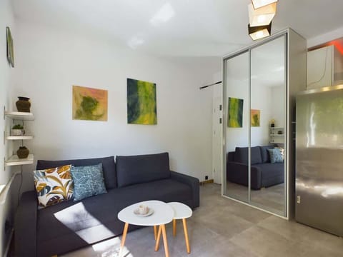 A cozy living room with a dark grey sofa, small round tables, and modern wall art. Natural light fills the space through a large window.