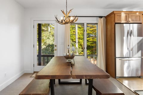 - Rustic dining area with live edge wood table and antler chandelier   - Natural light and forest views through sliding glass doors   - Perfect space for family dinners after mountain fun