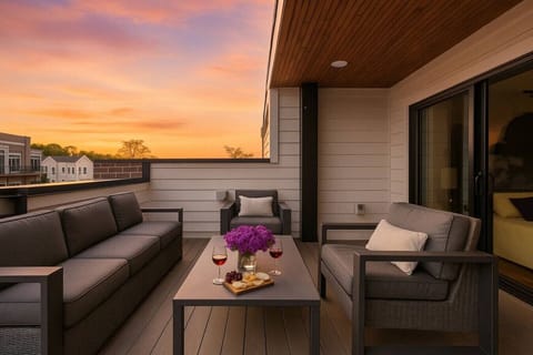 Rooftop terrace at golden hour with outdoor seating, a dining table, and purple flowers set against a warm sunset sky