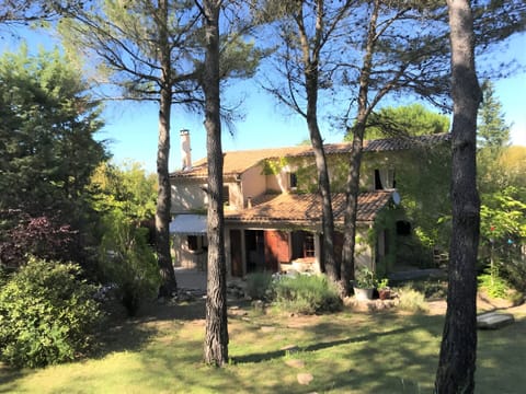 The villa is nestled amongst tall pine trees, offering privacy and a tranquil setting. The exterior of the house boasts a charming terracotta roof and a spacious garden with a glimpse of a patio. The home is surrounded by lush greenery, promising a peacef