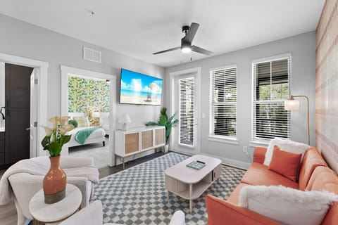 This is a modern and cozy living room featuring a vibrant orange sofa with tufted cushions, accented by a matching orange throw pillow and a soft white blanket
