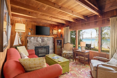 Cozy living space w/ plush seating, stone fireplace, and lake views through expansive windows.