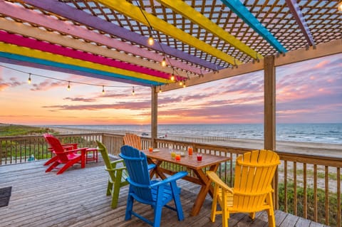 Beachfront deck with colorful pergola, outdoor dining table, and Adirondack chairs overlooking the Gulf at Gulf Drive, Galveston TX. Perfect sunrise and oceanfront vacation retreat.
