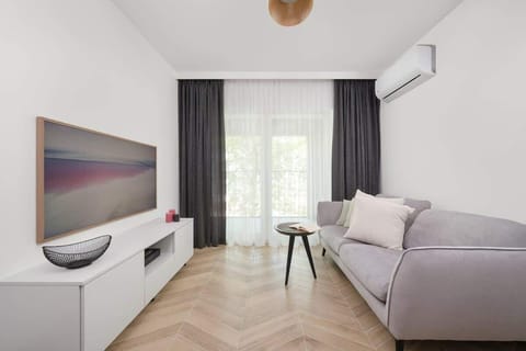 A cozy living room space with a sofa, TV, and large window letting in natural light. Perfect for relaxing or entertaining guests.