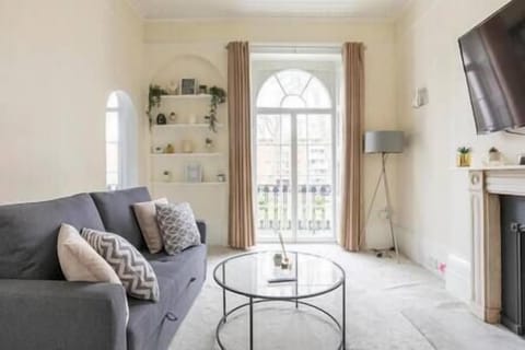 - Bright living room with sofa seating and smart TV  
- Large arched window with natural light and balcony view  
- Modern design with cozy decor and inviting atmosphere  

