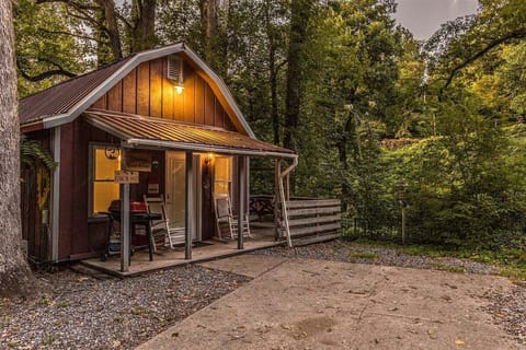 Exterior view of the red cabin with covered porch and gravel parking area surrounded by mature trees near Bryson City, NC. A secluded riverfront vacation rental in the Smoky Mountains.