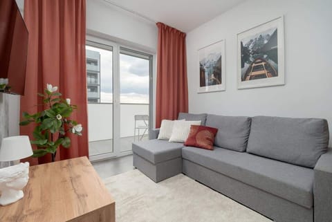 Bright living area with a gray sectional sofa, red curtains, and framed wall art.