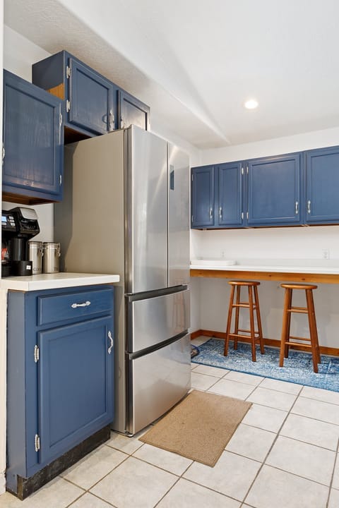Efficient kitchen w/ blue cabinets, stainless steel fridge & breakfast bar w/ stools.