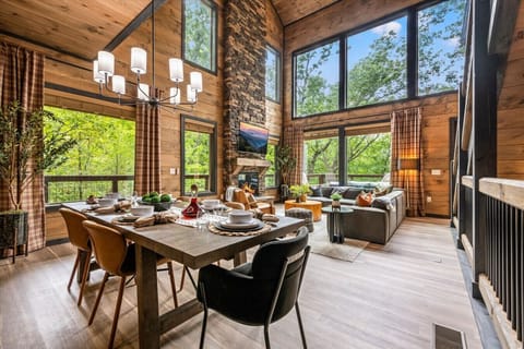 The breathtaking living area of Highland View includes large windows, a floor-to-ceiling stone fireplace, large Smart TV, comfortable furniture, dining table, and kitchen.