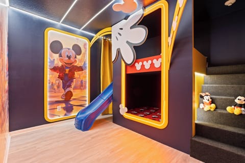Step into a fun-filled children's playroom adorned with vibrant colors and whimsical Mickey Mouse decor. The playful slide invites adventure, while cozy nooks and plush toys create a magical atmosphere perfect for young guests.