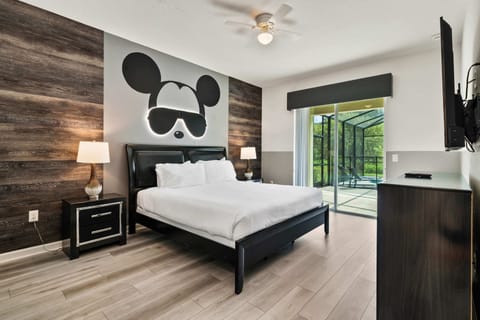 - King bedroom with sliding doors opening to poolside patio views  
- Modern décor and wood accent wall with playful Mickey artwork  
- Direct access to outdoor lounge area for convenient relaxation