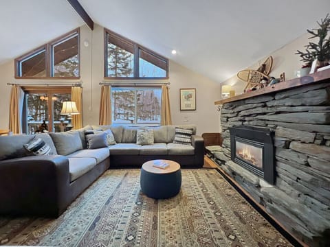Cozy main living space with stone fireplace and large windows overlooking the woods.