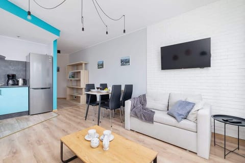 This modern living room features a clean white aesthetic with turquoise accents, stylish lighting, and a flat-screen TV mounted on a white brick wall.