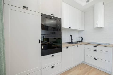 A minimalist kitchen area with white cabinets, a marble-style countertop, and modern appliances, including a built-in oven and sink.