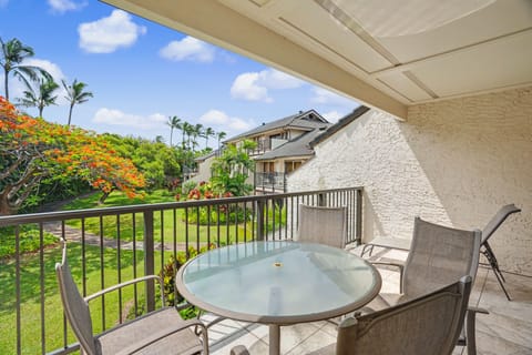 A covered balcony with garden and palm tree views, featuring a round glass dining table and comfortable seating—your perfect spot for morning coffee or sunset cocktails in the island breeze.