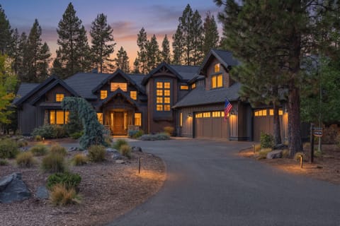 Striking mountain lodge exterior nestled among towering pines, photographed at dusk as warm lights illuminate its welcoming facade.