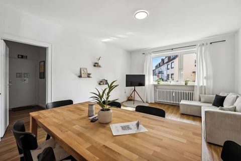 Heller, offener Essbereich mit natürlichem Licht, stilvoll eingerichtetem Holztisch und modernen Akzenten. Der Raum bietet gemütliche Sitzgelegenheiten und lädt zum Entspannen ein. Ideal für gesellige Mahlzeiten oder einen entspannten Abend.