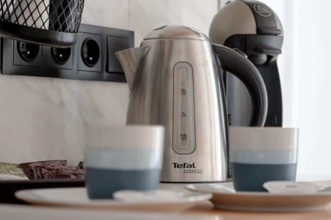 Close-up of a wooden countertop with an electric kettle, mugs, and coffee-making accessories.