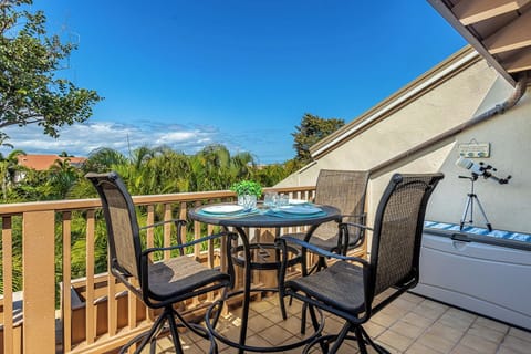 Sip your morning coffee at this private balcony table, surrounded by lush palm trees and tropical greenery under clear blue skies.
