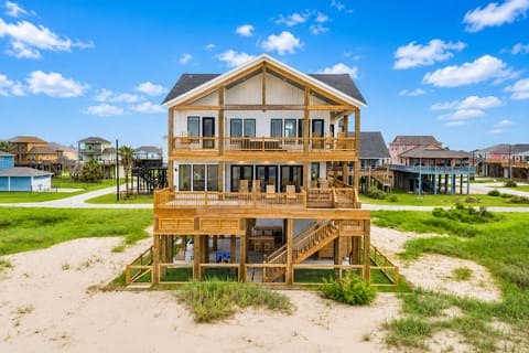 Full exterior view of the Bolivar Peninsula beach house showcasing expansive multi-level wooden decks, outdoor seating and sandy beachfront surroundings.